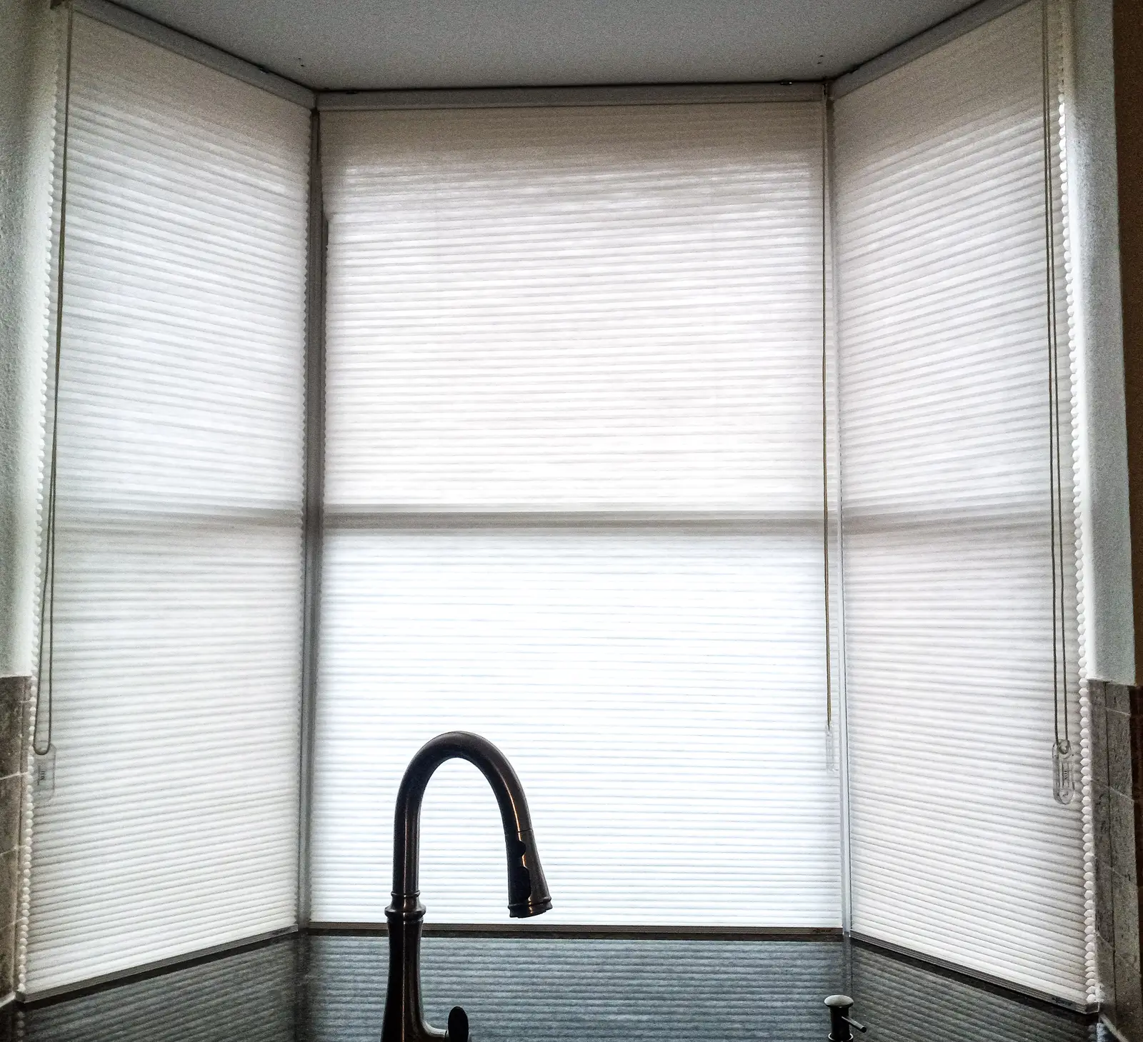 Honeycomb shades on a kitchen bay window above the sink