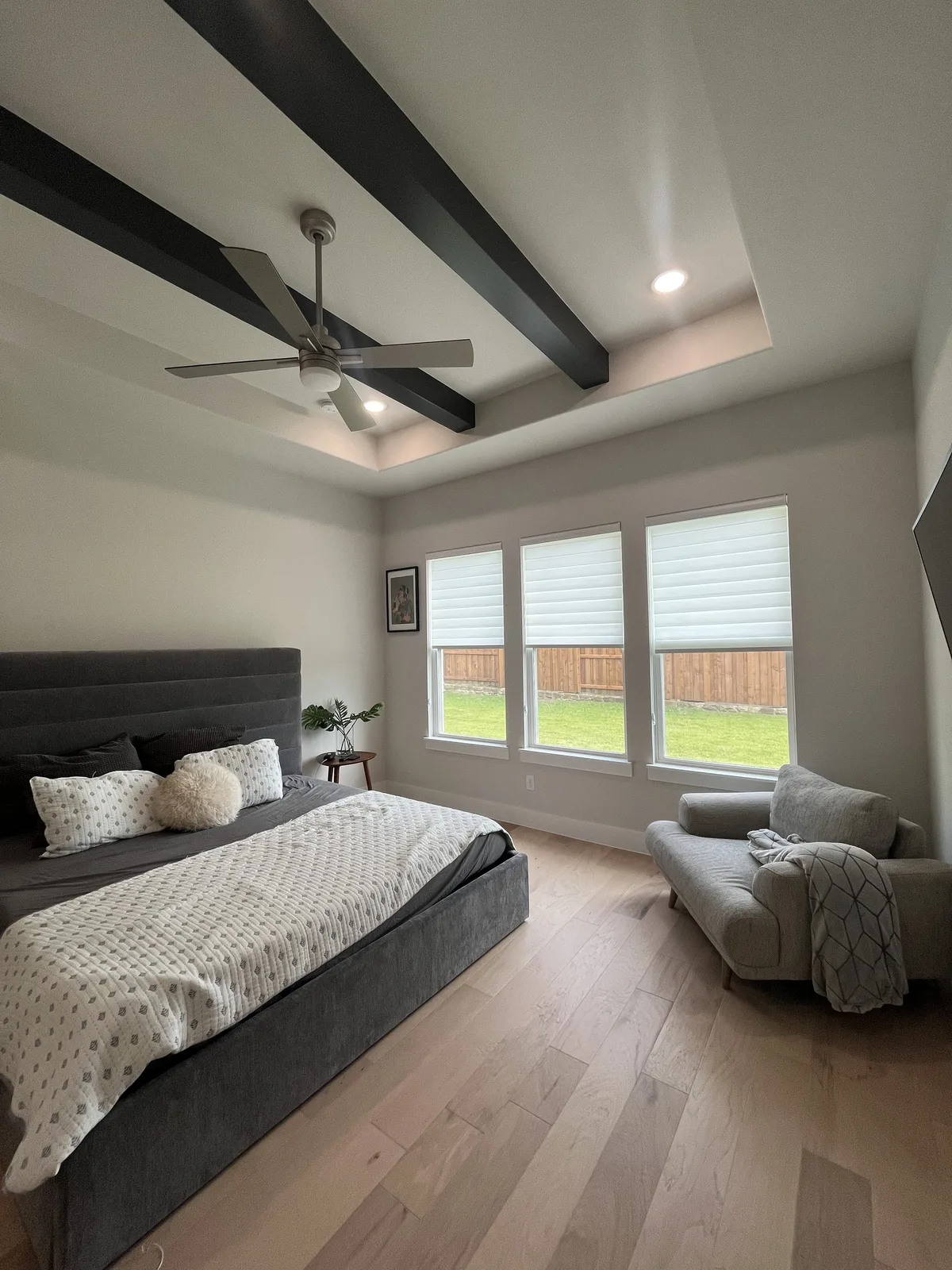 Triple shades in a master bedroom with wood beams